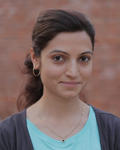 Apekshya Dhungel steht vor einem rötlichen Hintergrund und schaut lächelnd in die Kamera. 