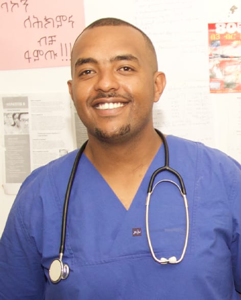 Surafel Mengistu trägt OP-Kleidung und lächelt in die Kamera. Um den Hals trägt er ein Stethoskop. 