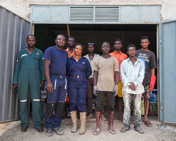 Isaac Asubonteng steht zusammen mit seinem Team vor einer Fabrikhalle. Einige der Personen tragen Arbeitskleidung und Handschuhe.